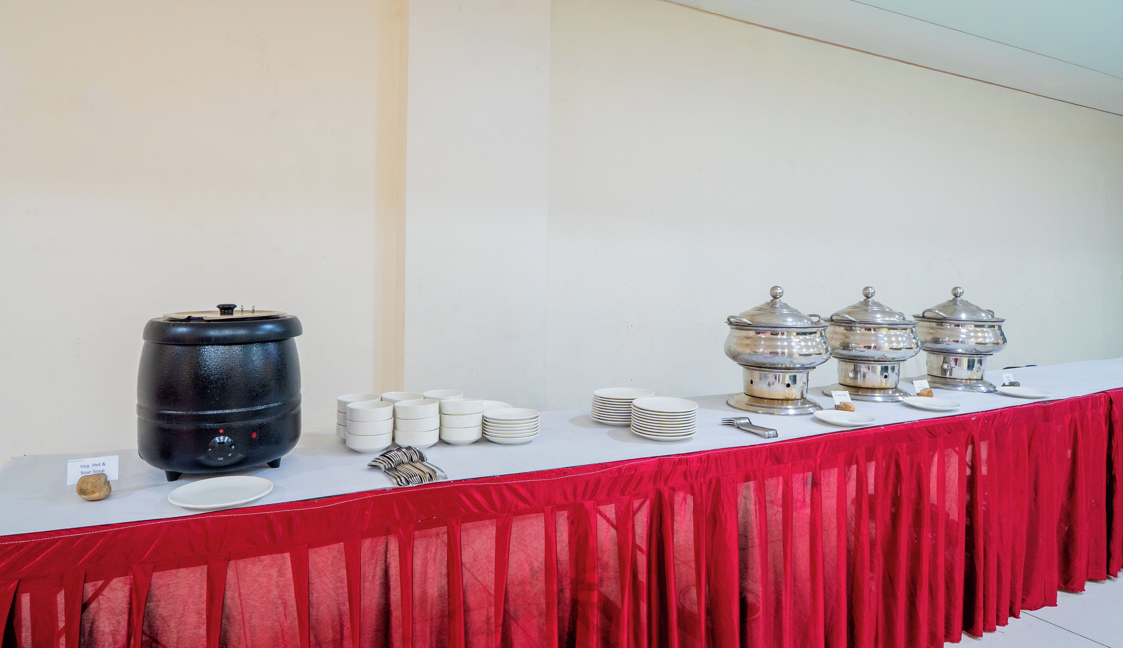 Un tavolo da buffet con tovaglia rossa, piatti bianchi, ciotole impilate e pentole d'argento per servire.
