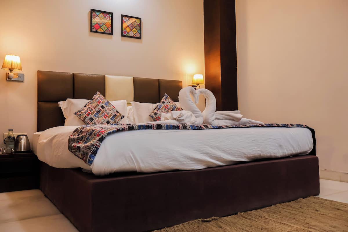 A neatly made bed with a patterned blanket and pillows, a dark headboard, and two wall-mounted lamps.