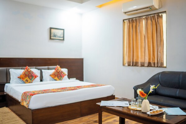 A hotel room with a bed, a sofa, a coffee table, and a window with curtains. - HHW Hotel- Agra (Agra)