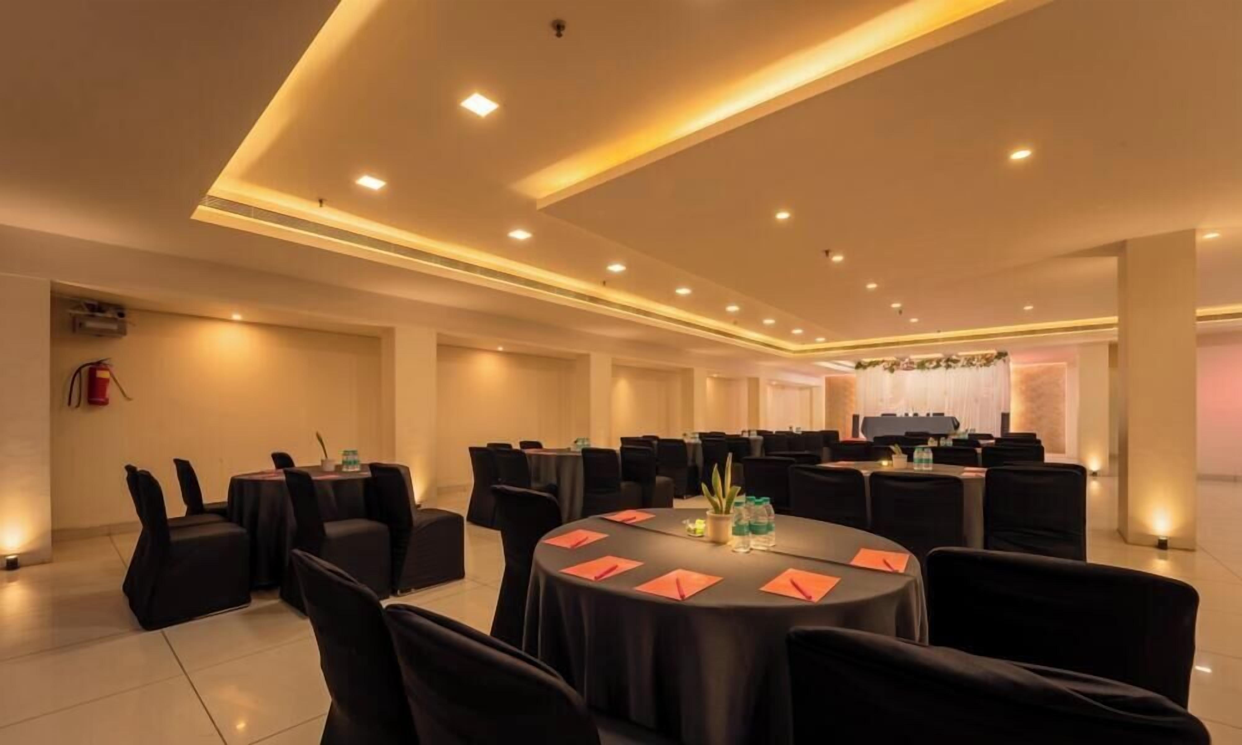 A conference room with round tables, black chairs, and a stage with a floral backdrop.