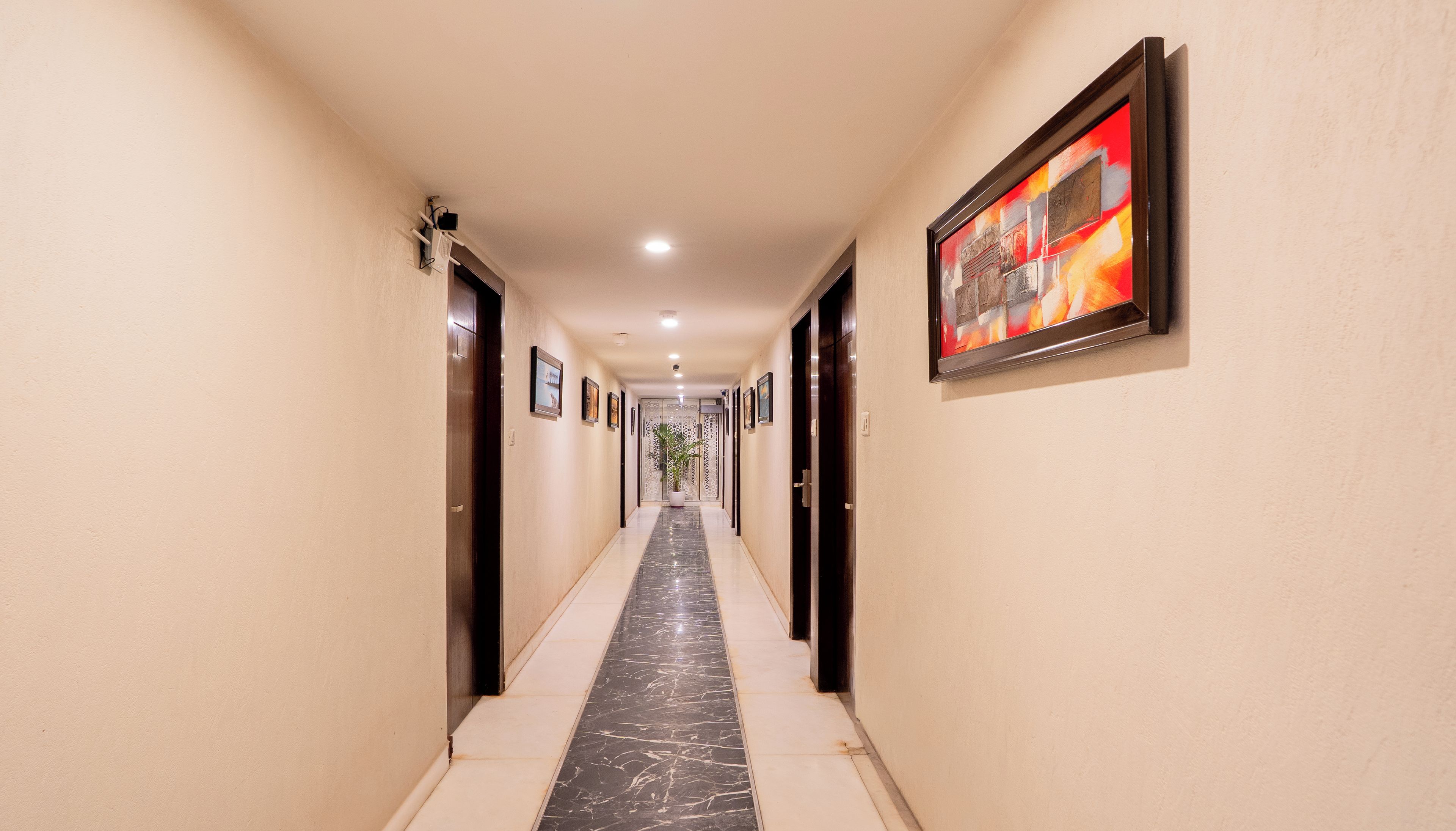 A hotel hallway with doors on both sides, a marble floor, and framed artwork on the walls.