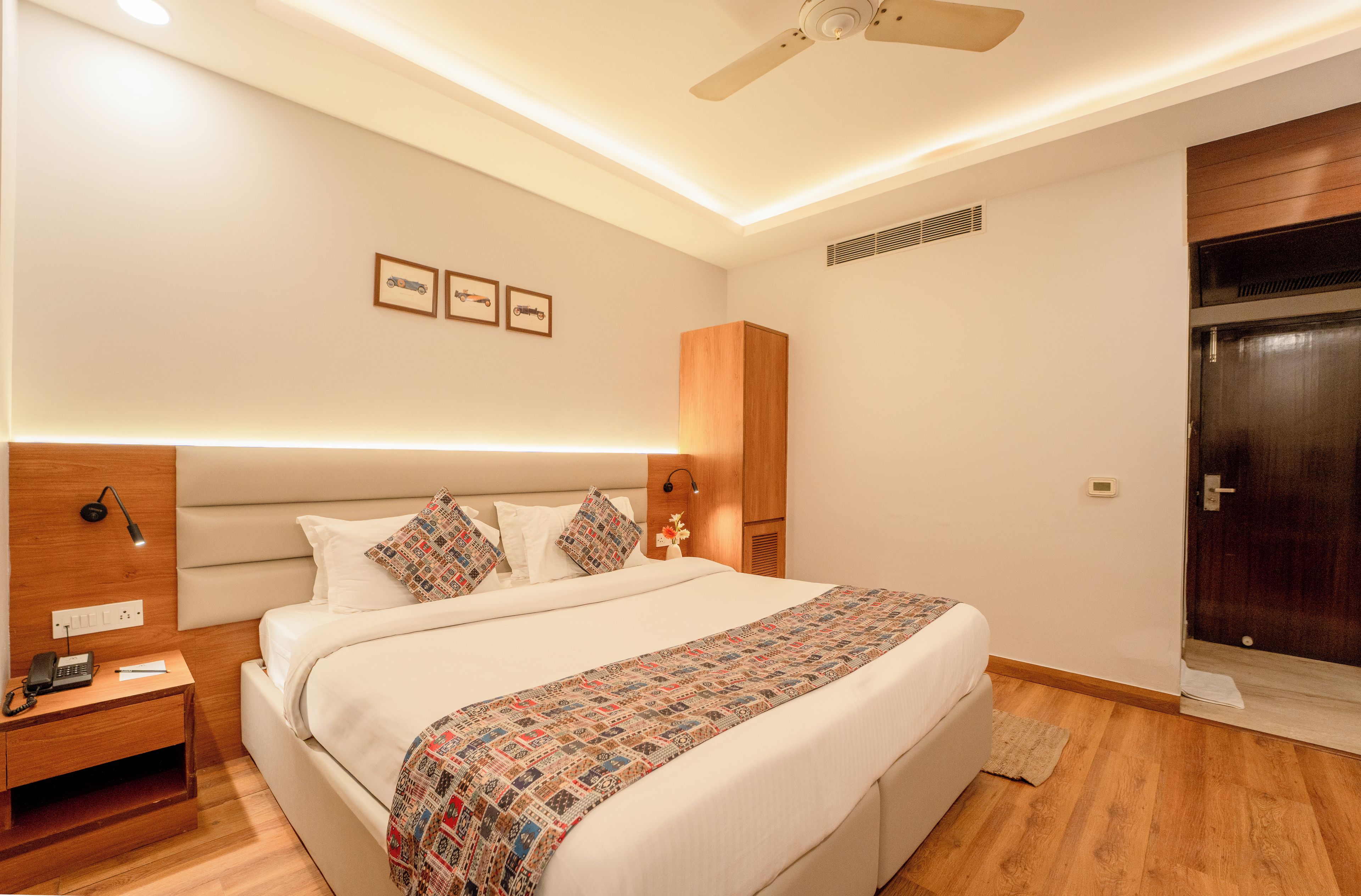 Een hotelkamer met een bed, nachtkastje, lamp, kunstwerk aan de muur en een plafondventilator.