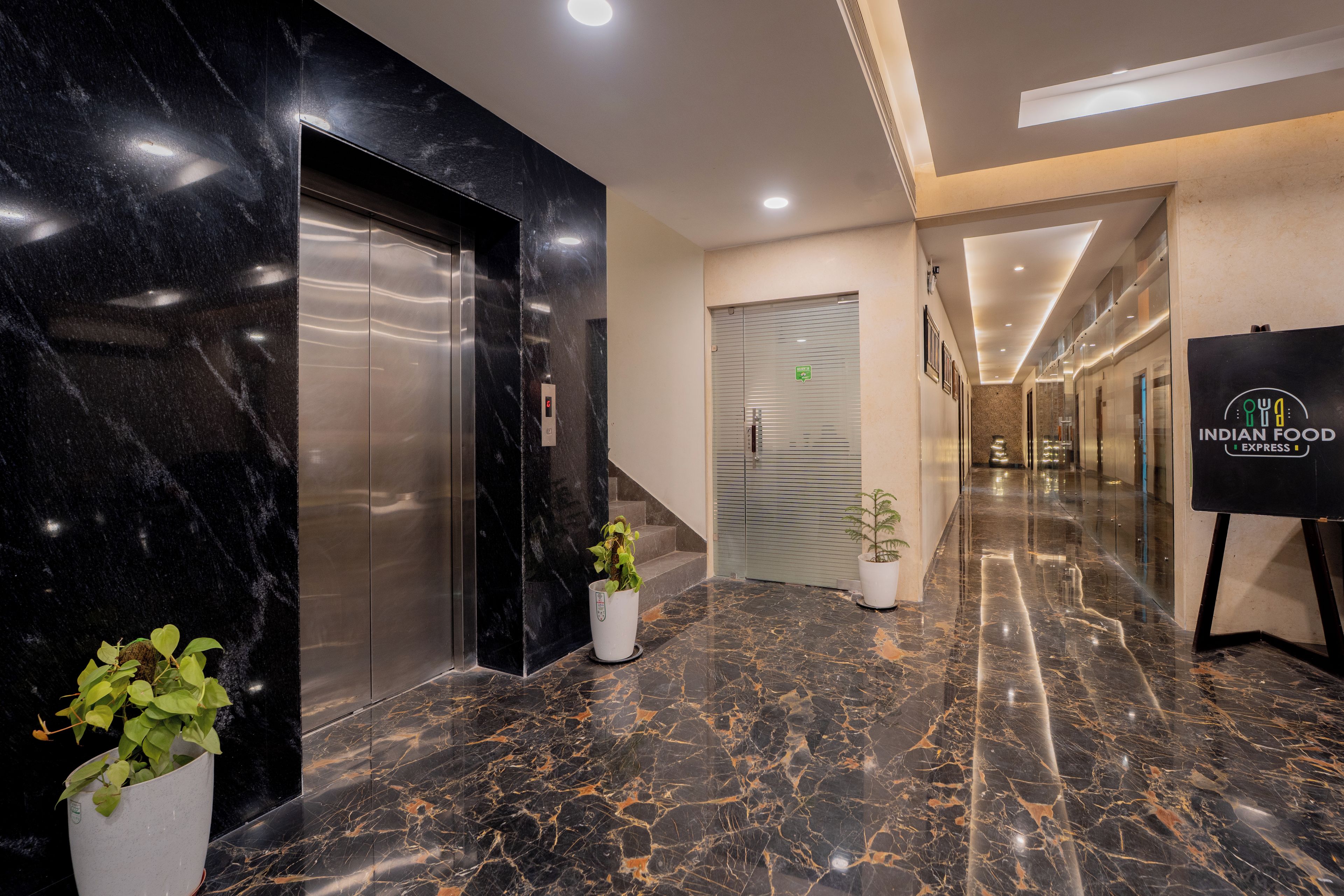 Vestíbulo de hotel con piso de mármol, ascensores, una escalera y un letrero que anuncia comida india.