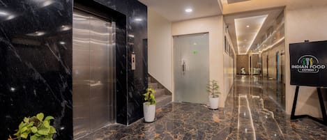 Vestíbulo de hotel con piso de mármol, ascensores, una escalera y un letrero que anuncia comida india.