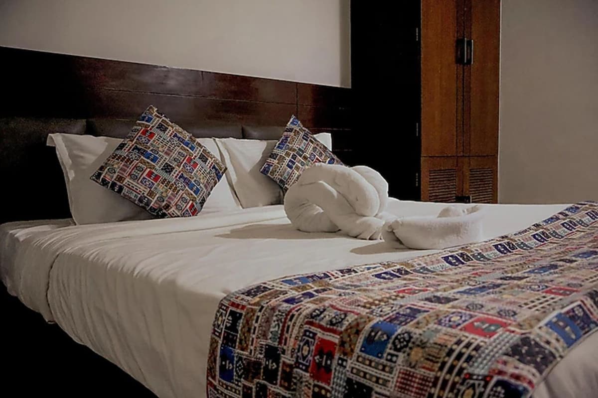 A neatly made bed with patterned pillows and a quilt, a wooden headboard, and a wooden wardrobe.