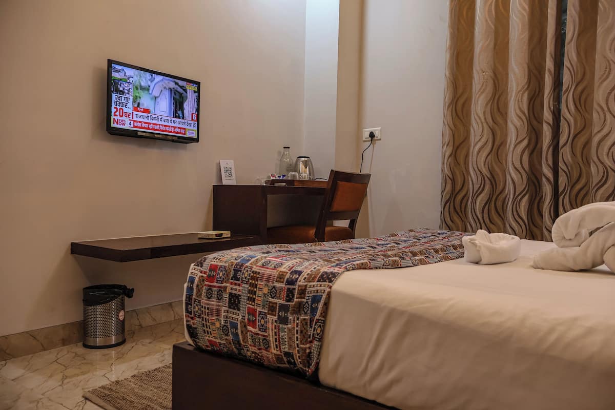 A hotel room with a bed, a desk with a chair, a television mounted on the wall, and a patterned bedspread.