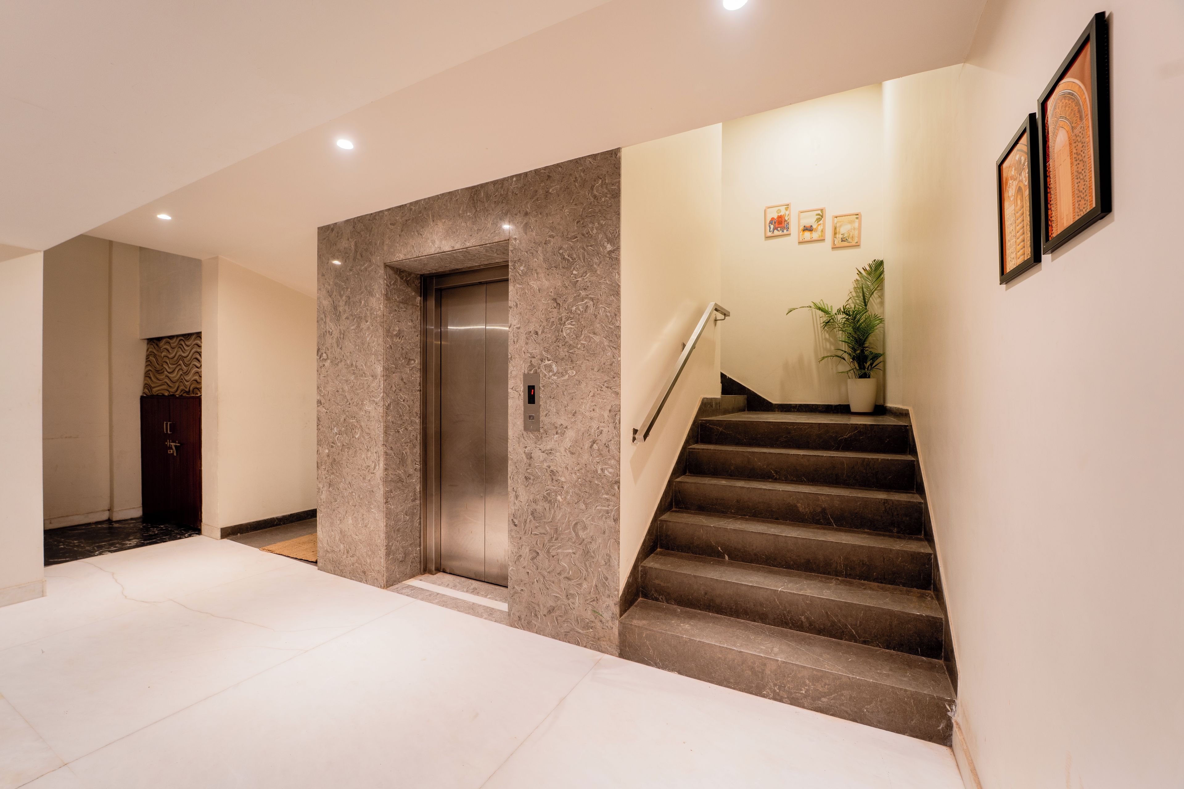 A modern interior with a marble wall, an elevator, a staircase, and a potted plant.