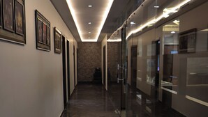 A hallway with a marble floor, framed artwork on the walls, and glass partitions with display cases. - HHW Hotel- Agra (Agra)
