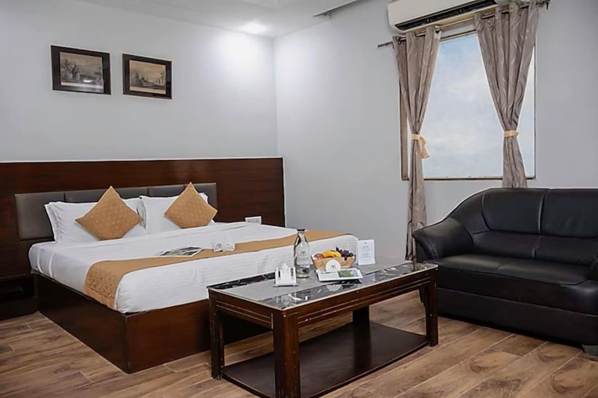 Une chambre d’hôtel avec un lit, une table basse, un canapé en cuir noir et une fenêtre avec des rideaux.