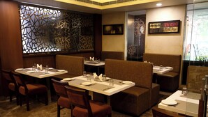 A restaurant with booths and tables, each set with plates, glasses, and cutlery. - HHW Hotel- Agra (Agra)