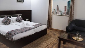 A hotel room with a bed, a black leather sofa, a glass coffee table, a view of a cityscape through a window, and a framed picture on the wall. - HHW Hotel- Agra (Agra)