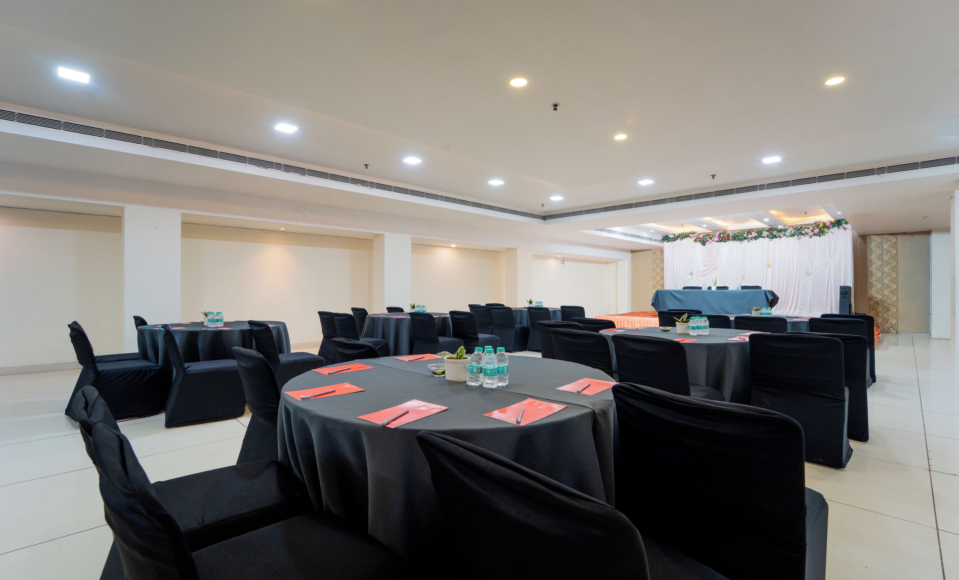 Sala de conferência com várias mesas e cadeiras, equipada com garrafas de água e placas de identificação.