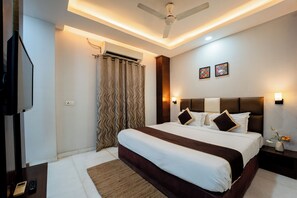 Una camera d'albergo con un letto, una televisione, una ventola a soffitto e un condizionatore d'aria a parete.