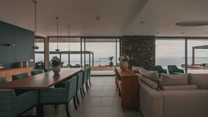 A modern living room with a large wooden dining table, green upholstered chairs, a beige sofa, and a stone accent wall.