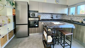 Une cuisine moderne équipée d’un réfrigérateur, d’un four, d’un four à micro-ondes et d’une cuisinière à gaz. On y trouve également un petit îlot avec des tabourets et une fenêtre au-dessus de l’évier.