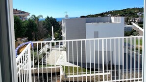 Un balcon avec une balustrade blanche, un ciel d’un bleu limpide et une vue sur un quartier résidentiel avec des immeubles et de la verdure.