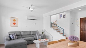 A modern living room with a grey sofa, a round coffee table, and a wooden dining table with a vase of flowers.