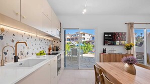 A modern kitchen with white cabinets, a granite countertop, and a built-in sink. There is a dining area with a wooden table and chairs, and a large window offering a view of the surrounding buildings.