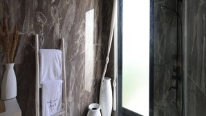 A modern bathroom with a marble wall, a glass shower enclosure, and a white towel rack. - Lilla Villa by Betterplace (Canggu)