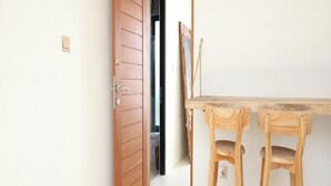 A room with a wooden door, a table, and two wooden stools. - Lilla Villa by Betterplace (Canggu)