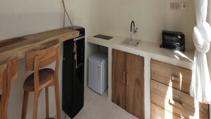 A compact kitchen with a wooden table, a small refrigerator, a sink, and a microwave. - Lilla Villa by Betterplace (Canggu)