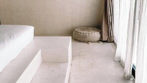A minimalist room with a bed, a small round ottoman, and a curtain. - Lilla Villa by Betterplace (Canggu)