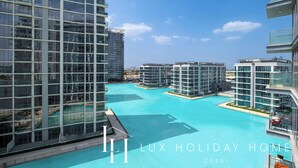 A modern high-rise building with a large swimming pool surrounded by other high-rise buildings. - LUX | 2BR Lagoon View – District One, 10–15 min Burj Khalifa (Dubai)