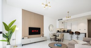 A modern living room with a flat-screen TV, a dining area, and a kitchen. - LUX | 2BR Lagoon View – District One, 10–15 min Burj Khalifa (Dubai)