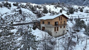 A wooden chalet with a balcony, set in a snowy mountainous area.