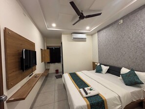 A hotel room with a bed, a TV mounted on a wooden panel, a ceiling fan, and an air conditioning unit.