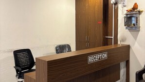 En receptionsdisk med träpanel och marmorfot, en svart kontorsstol, ett träskåp och en väggmonterad fläkt.