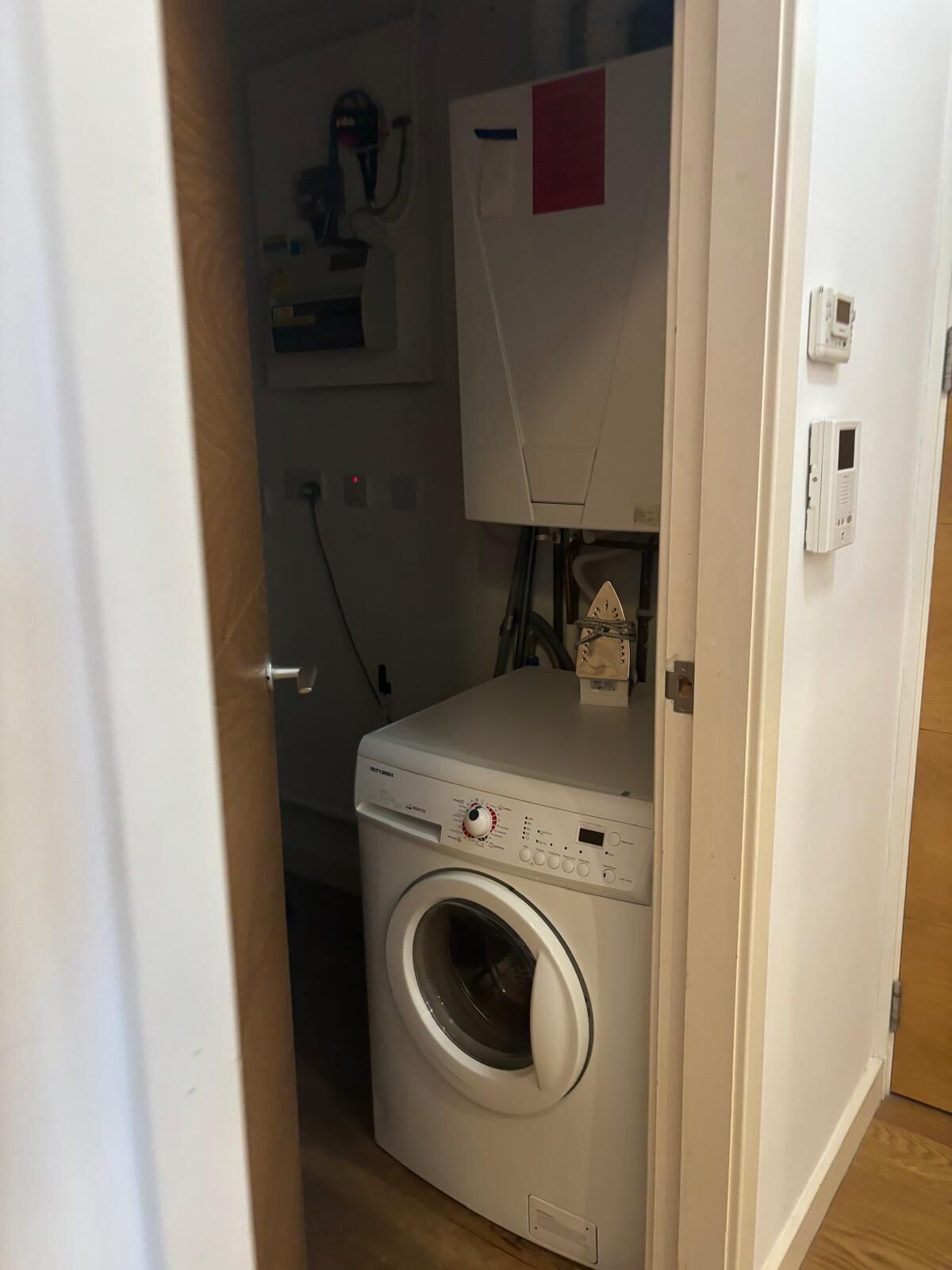 A compact laundry room with a front-loading washing machine, a small heater, and a control panel.