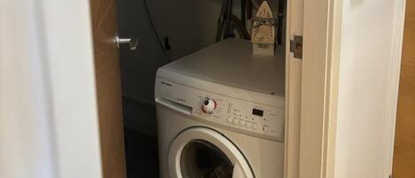 A compact laundry room with a front-loading washing machine, a small heater, and a control panel.