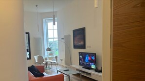 Moderni olohuone, jossa on lasinen sohvapöytä, punainen sohva, litteänäyttöinen televisio sekä ruokailutila, jossa on lasipöytä ja -tuolit.