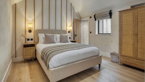 A bedroom with a large bed, wooden headboard, two bedside tables with lamps, a wardrobe, and a window with blinds. - Coastal Penthouse, Panoramic Sea View Apartment (The Mumbles)