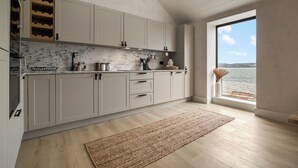 A modern kitchen with white cabinets, a marble backsplash, and a view of the sea through a large window. - Coastal Penthouse, Panoramic Sea View Apartment (The Mumbles)