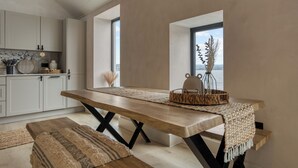 A modern kitchen with a large wooden table, white cabinets, and a view of the water. - Coastal Penthouse, Panoramic Sea View Apartment (The Mumbles)
