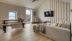 A spacious living area with a wooden floor, a sofa, a table, and a TV mounted on the wall. - Coastal Penthouse, Panoramic Sea View Apartment (The Mumbles)