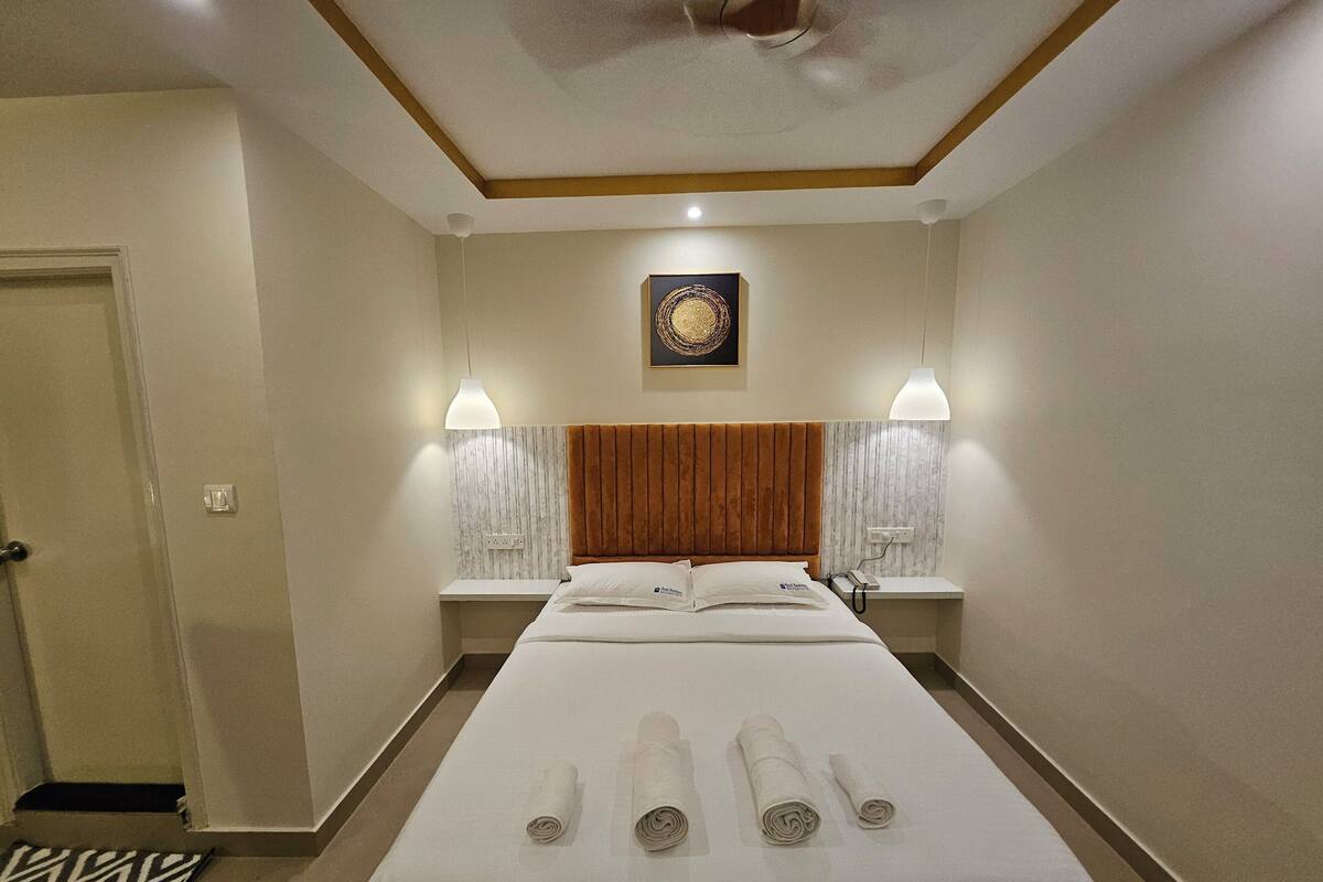 A hotel room with a large bed, two bedside tables, a ceiling fan, and a wall-mounted artwork.
