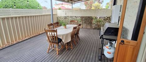 A covered outdoor patio with a wooden table and chairs, a grill, and a propane tank.