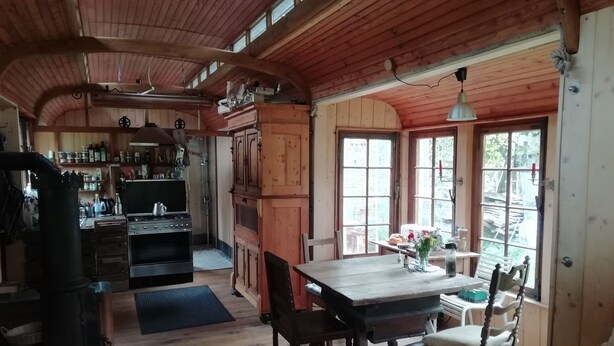 A rustic wooden interior with a kitchen, dining area, and large windows. - Circus wagon star tent with sauna. Very spacious with pavilion. (Windeck)