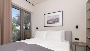 A modern bedroom with a large bed, a framed picture on the wall, and a view of trees through the window. - AdeLis Residence (Piran)