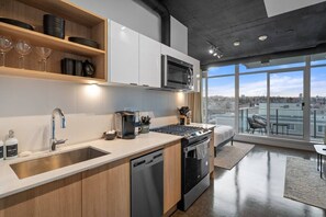 Una cocina moderna con lavavajillas, microondas y estufa, un comedor con mesa y sillas, y un amplio ventanal con vistas a la ciudad.