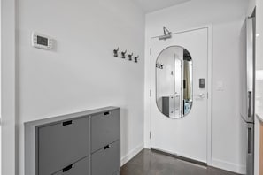 Un pasillo con una puerta blanca, un espejo redondo, un termostato y un armario gris.