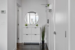 A hallway with a white door, a round mirror, a white cabinet with two drawers, and a potted plant.