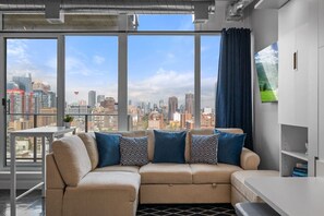 A modern living room with a sectional sofa, a dining table, and a large window offering a city view.