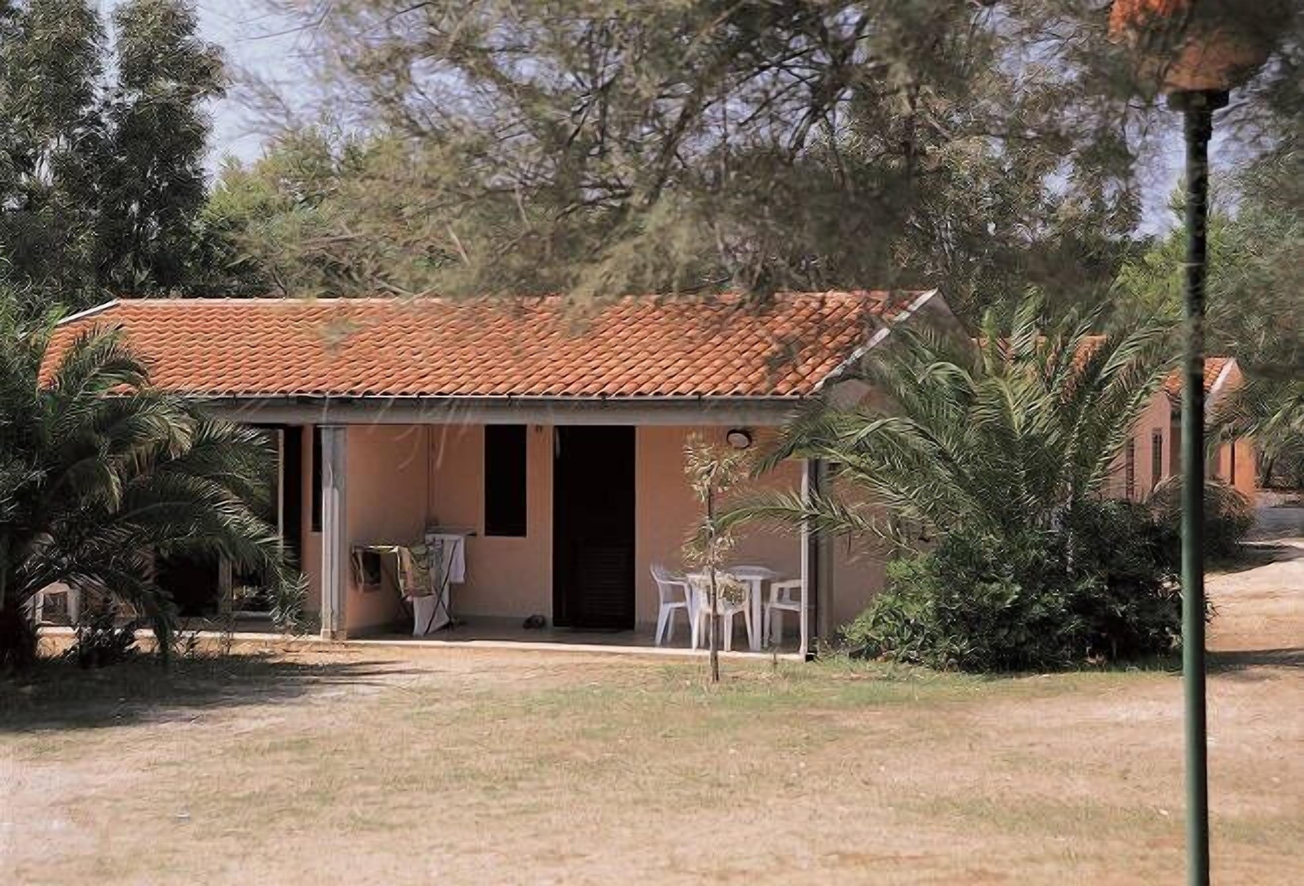 A small building with a tiled roof, a door, and a small patio area with chairs.