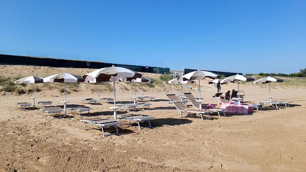 Une plage avec des chaises longues et des parasols, une table rose et un ciel dégagé.