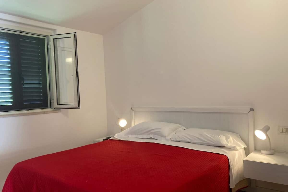A single bed with a red bedspread, white pillows, and two bedside lamps.