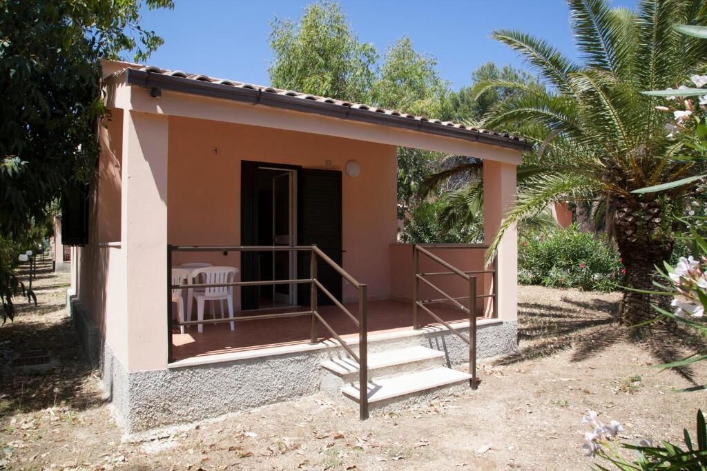 Een klein gebouw met een overdekte veranda, een deur en een trap naar een terras.